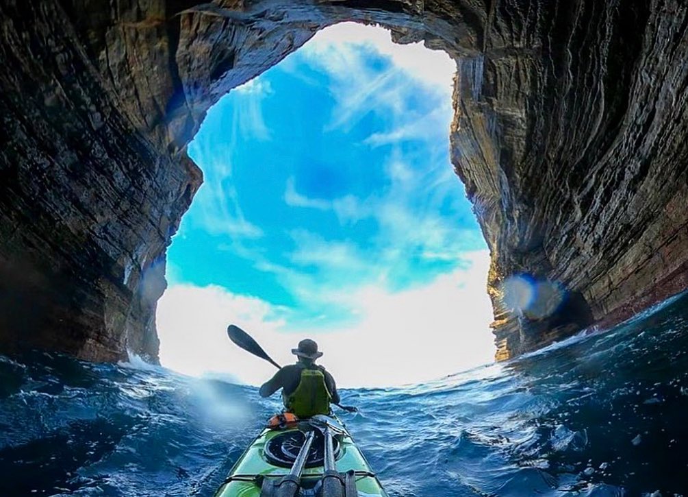 Picture of Kayak paddler going through a hole in the rocks wearing a shelta sun hat