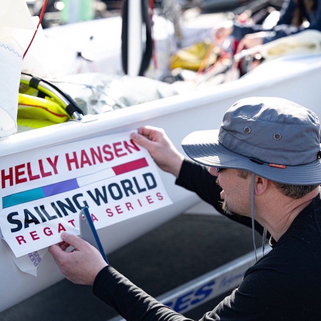 Picture of man putting a bumper sticker on boat for the Helly Hansen Sailing World Regata series. Wearing a Shelta Sun Hat