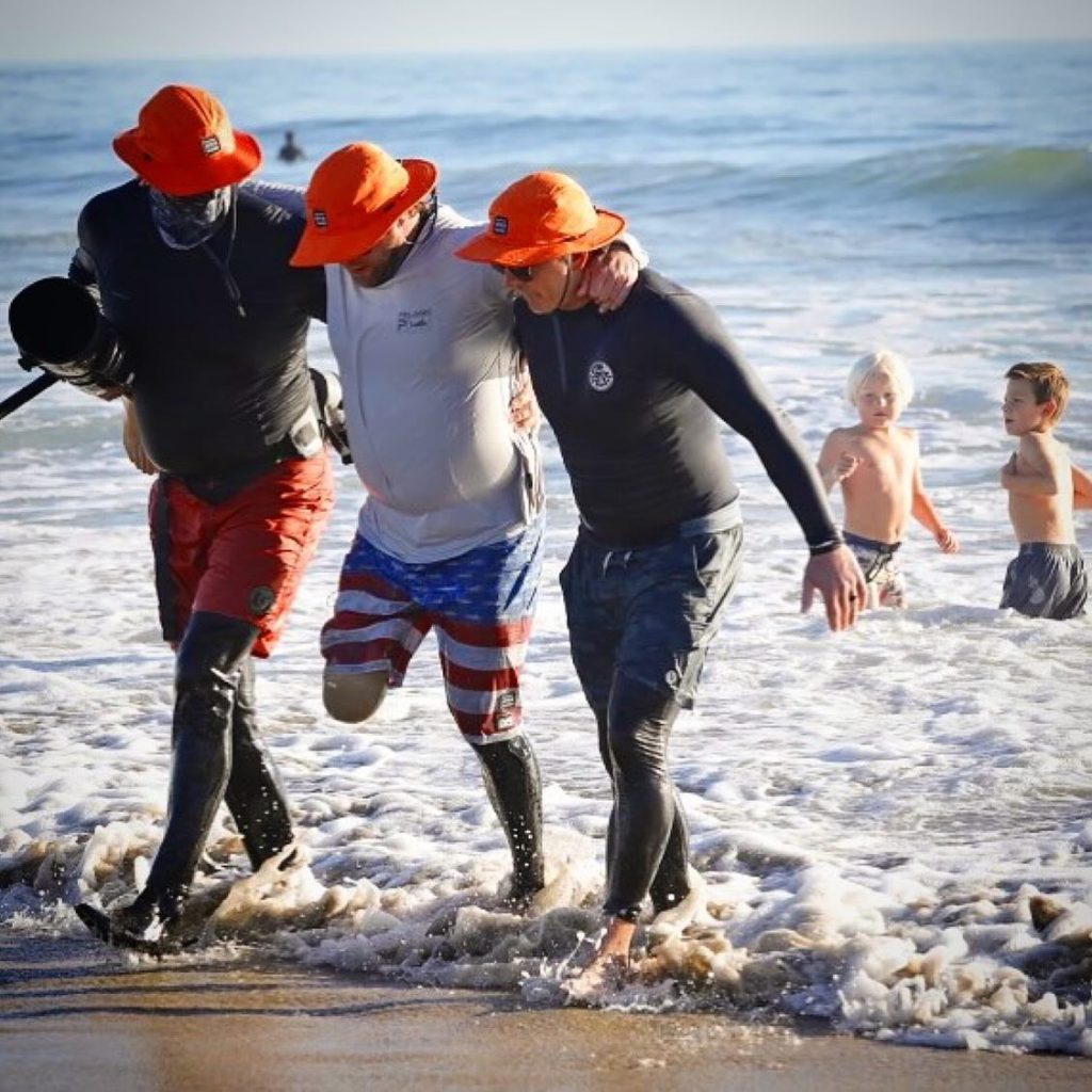 Picture of Two men helping an veteran with one leg getting out of the water. All wearing Shelta Sun Hats